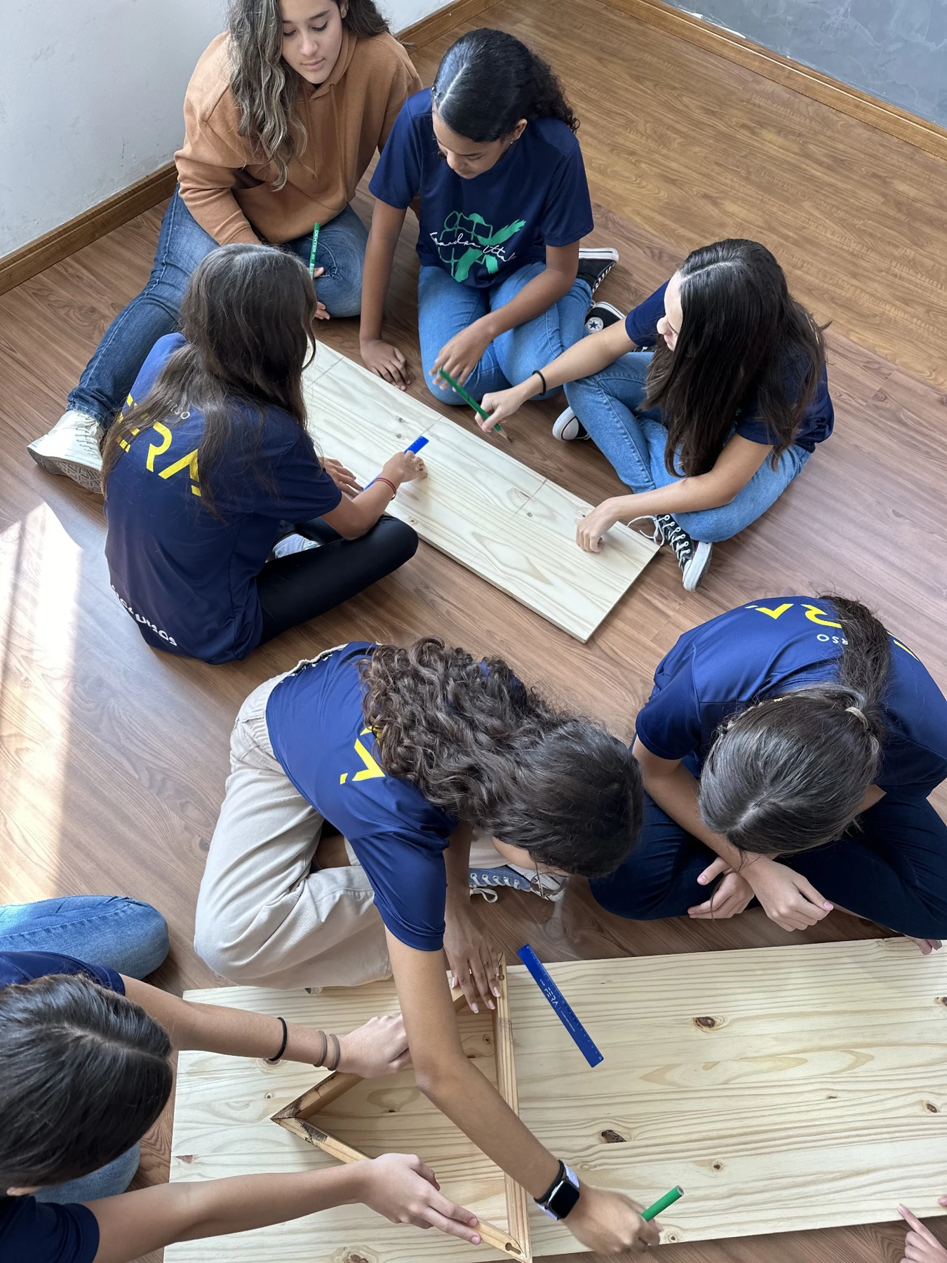 Alunos de 7º ano no chão da sala, trabalhando em grupo com peças de madeira